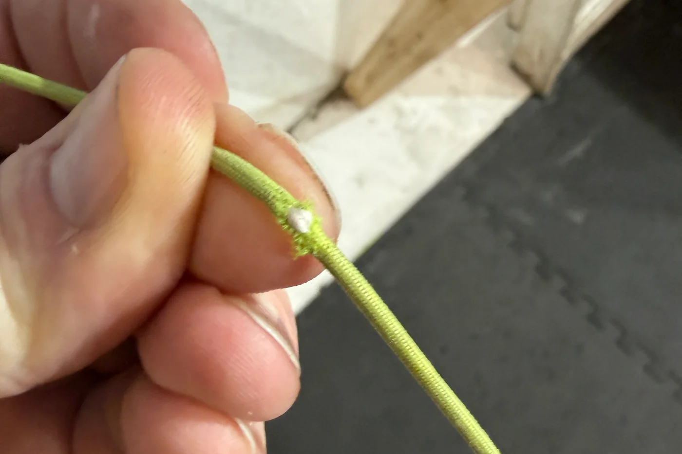A damaged green paraglider line held for inspection, with its white core exposed