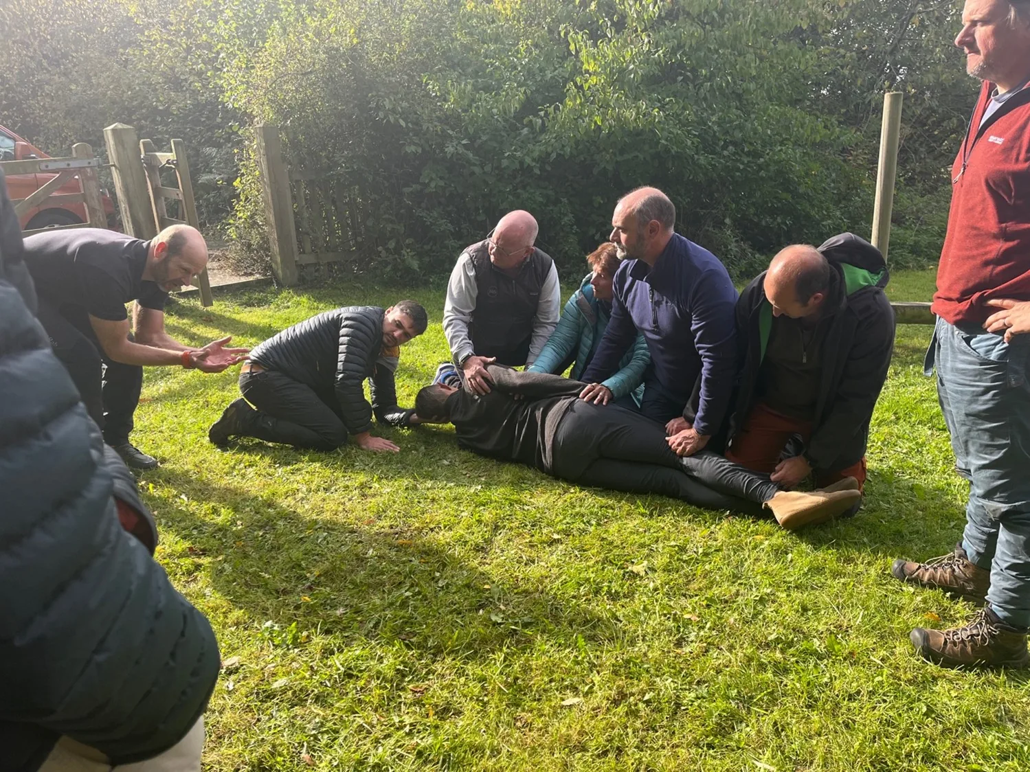 First aid trainees kneeling around a participant lying on the grass during an outdoor exercise
